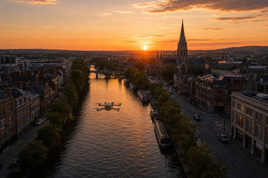 A drone hovering over a river running through a city centre at sunset