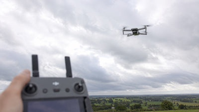 A pilot holding the controller while keeping the drone in sight against a cloudy sky