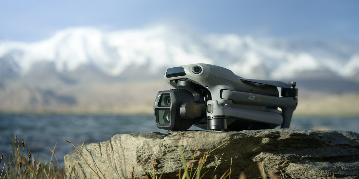 A DJI Air 3S folded on a rock, snow covered mountains behind