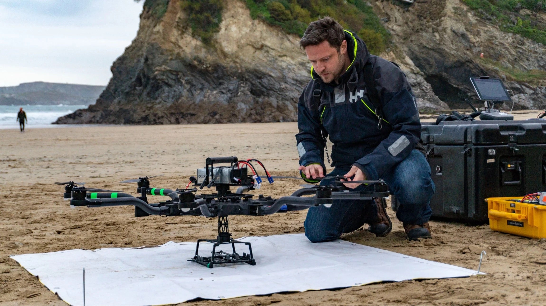 Matt Williams kneeling beside a Freefly Alta 8 on a beach landing mat, cliffs behind